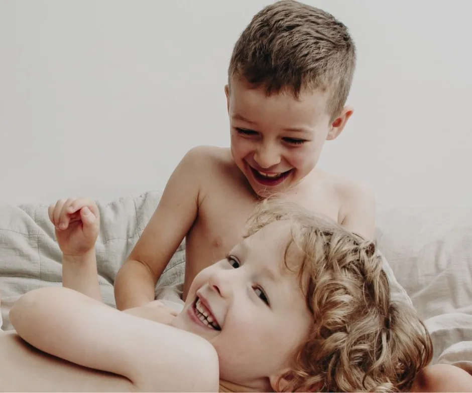 Two children laughing together on a bed